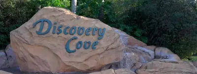 Large stone sign reading "Discovery Cove" surrounded by lush green vegetation