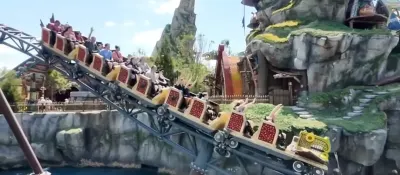 Roller coaster ride with passengers in themed fantasy setting with stone structures