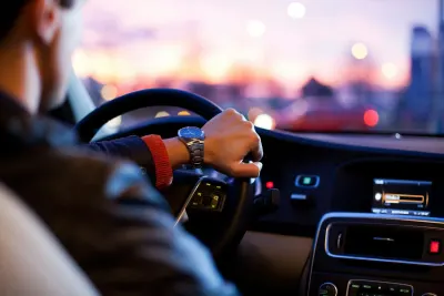 Driver wearing watch and red sleeve at steering wheel during sunset