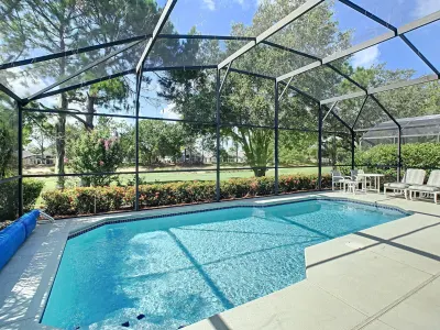 Screened pool enclosure with crystal blue water and lanai furniture overlooking manicured lawn