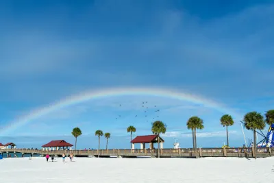 Rainbow arching over Clearwater Beach pier with palm trees and visitors on sand