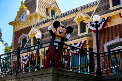 Mickey Mouse waves from a Victorian-style building with a clock tower at Disney World