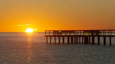 Wooden pier silhouetted against golden sunset over calm ocean waters