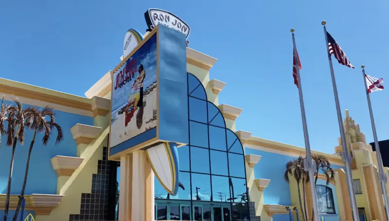 Ron Jon Surf Shop storefront with yellow exterior, large sign, and flagpoles under blue sky